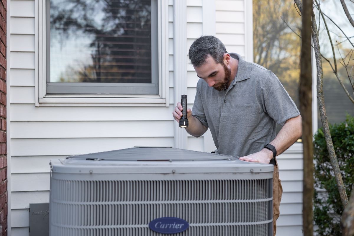 A heating engineer inspecting an outdoor heat pump unit at a house